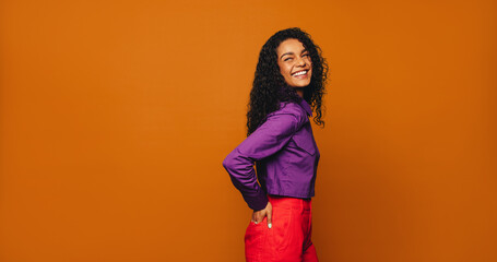 Vibrant woman with curly hair and fashionable style standing on a bright orange background