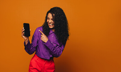 Cheerful woman recommending a colourful mobile device on a vibrant orange background