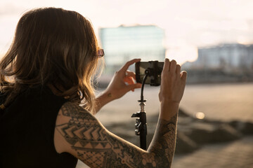 Young woman with tattoos taking pictures or shooting video with her phone