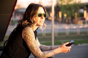 Young business woman with piercings and tattoos looking at the distance and holding a phone