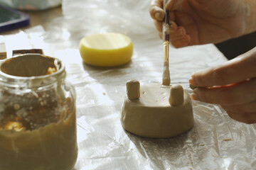 A woman makes a small flower pot from clay and works with a brush.