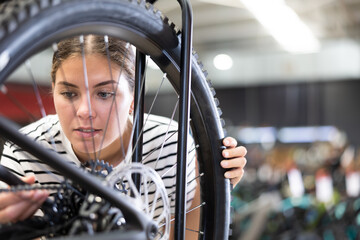 Enthusiastic young female cyclist examining bike wheel system in store while choosing combination...