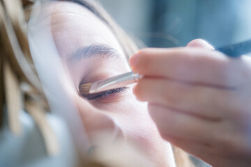 Detail of the reflection of a young teenager in a small vanity mirror applying eye makeup with a...