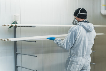 man in respirator mask putting painted wooden planks on shelves in carpentry shop. High quality...
