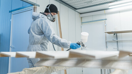 Carpenter in his paint room spraying a piece of wood to be used in his workshop later. High quality...