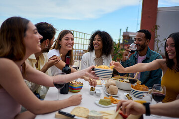 Group of multi-ethnic young friends enjoying meal gathered on rooftop. Happy millennial people having fun drinking red wine and eating celebrating a party event on summer day - Powered by Adobe