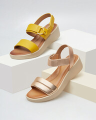 Stylish women sandals in vibrant yellow and elegant rose gold, artistically on white cubic props...