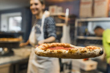 focus on the baked pizza holding by a woman cook with a peel in the bakery. High quality photo