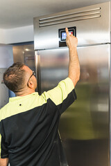 man adjusting fridge setting in the kitchen, saving products in the restaurant kitchen. High quality photo