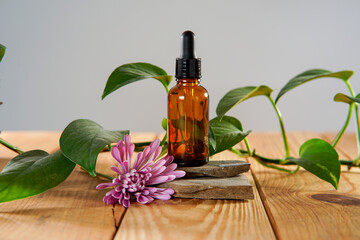 A bottle of essential oil sitting on rocks on  a natural wooden table with a pink dahlia on the side.