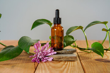 A bottle of essential oil sitting on rocks on  a natural wooden table with a pink dahlia on the side.