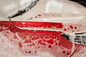 Closeup of red car foamed by liquid, resembling vibrant carmine artwork