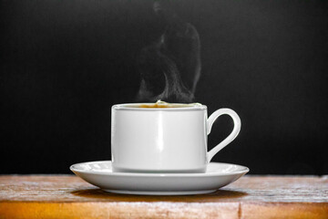 Minimalist cup of tea coming out of smoke on wooden surface and dark background.