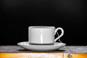 Minimalist cup of tea coming out of smoke on wooden surface and dark background.