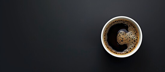 A white glass contains black coffee, set against a black backdrop, captured from above with space...