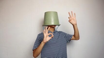 young man using a bucket on his head on a white background. showing okay gestures