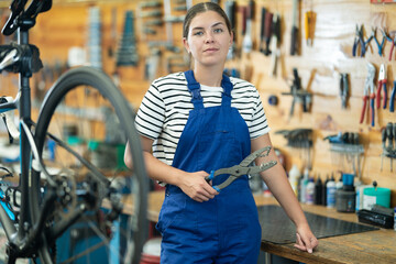 Young woman bicycle repair service worker in uniform posing with tool