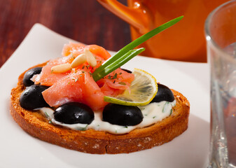 Slices of salmon and black olives served on toasted baguette with cream sauce on white plate..