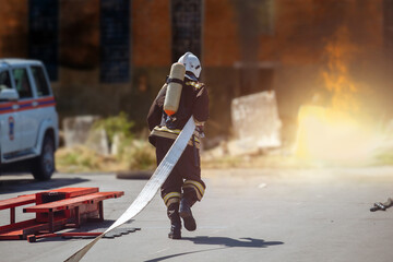 Firefighter with hose running to burning industrial building