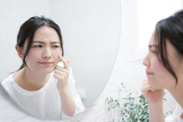 Woman concerned about the texture of her skin while looking in the mirror Image of skin care and beauty Concerns about skin tone Acne and pimples