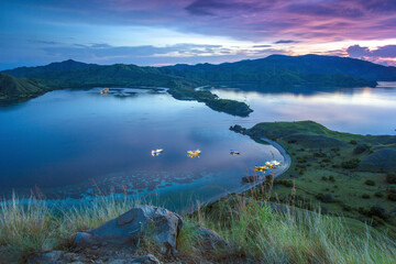 view of the sea surrounded by hills with green grass with a dark green sea color and there are several boats sailing with the nuances of the sun on Gili Lawa land © Abdurrahman