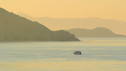 view of the sea and hills with a yellowish sky and a ship in the middle of the sea sailing on Gili Lawa land © Abdurrahman