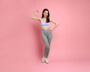 Happy young woman with slim body showing her muscles on pink background