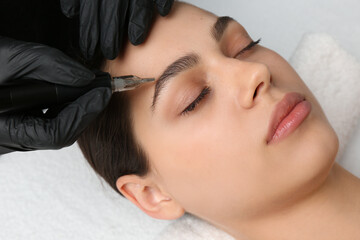 Beautician making permanent eyebrow makeup to young woman, closeup