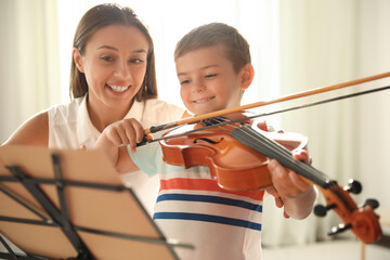 Young woman teaching little boy to play violin indoors
