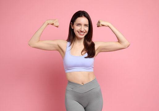 Fototapeta Happy young woman with slim body showing her muscles on pink background
