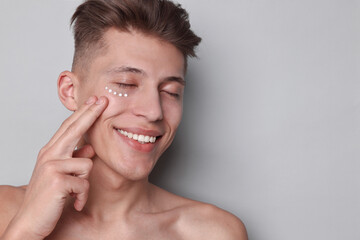 Handsome man with moisturizing cream on his face against light grey background. Space for text
