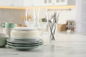 Many different clean dishware and glasses on white marble table in kitchen. Space for text