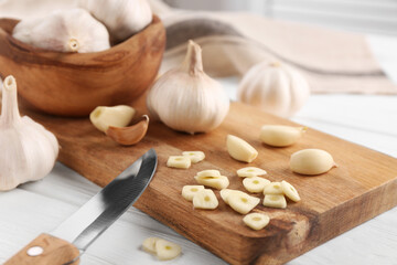 Aromatic cut garlic, cloves, bulbs and knife on white wooden table, closeup