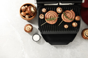 Electric grill with homemade sausages, rosemary and mushrooms on marble table, flat lay. Space for text