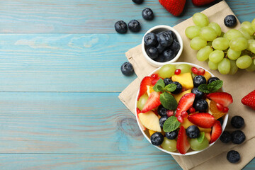 Tasty fruit salad in bowl and ingredients on light blue wooden table, flat lay. Space for text