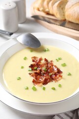 Tasty potato soup with bacon in bowl and spoon on white table, closeup