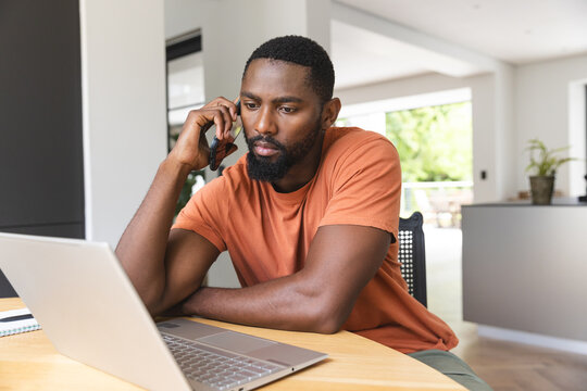 At home, African American male homeowner wearing an orange shirt, talking on phone - Powered by Adobe
