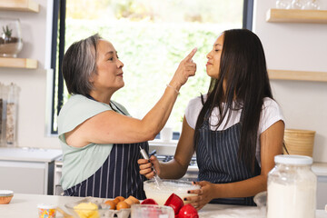 Asian grandmother with visible wrinkles is touching biracial teenage granddaughter's nose at home
