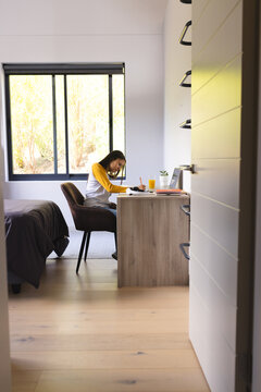 Biracial young woman wearing glasses, writing at desk at home
