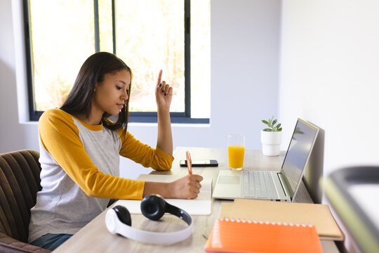 Biracial young female raising hand during video call at home