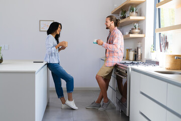 Biracial woman and Caucasian man, couple, enjoying coffee in kitchen at home