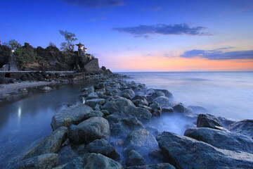 lots of rocks lined up near the misty sea water with sunset nuances with slightly purplish and yellowish colors and black clouds at Batu Bolong Temple, Lombok