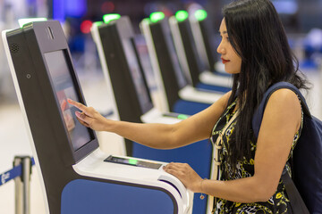 Young woman using self check-in kiosks in airport terminal.