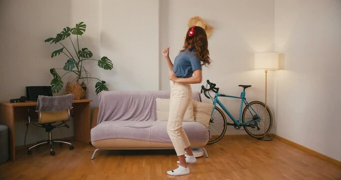 Happy Latin woman dances while robot cleaner hoovers floor