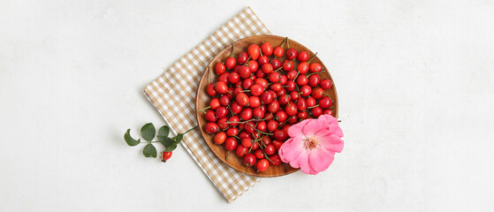 Wooden plate with fresh rose hip berries and flower on white background