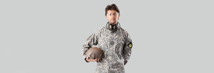 Young male soldier with helmet on grey background