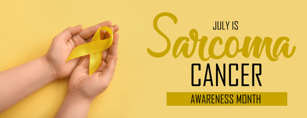Hands with golden ribbon on yellow background. Children cancer awareness concept