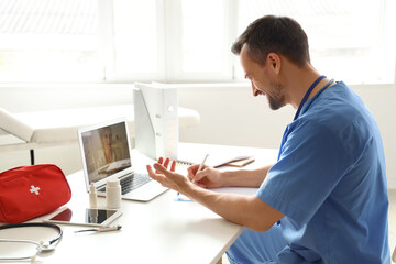 Handsome doctor video chatting with patient on laptop in office
