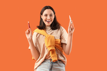 Happy young woman with electronic cigars on orange background
