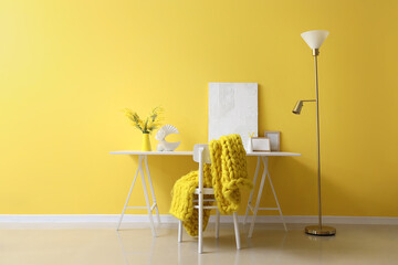 Stylish workplace with decor and beautiful mimosa flowers near yellow wall